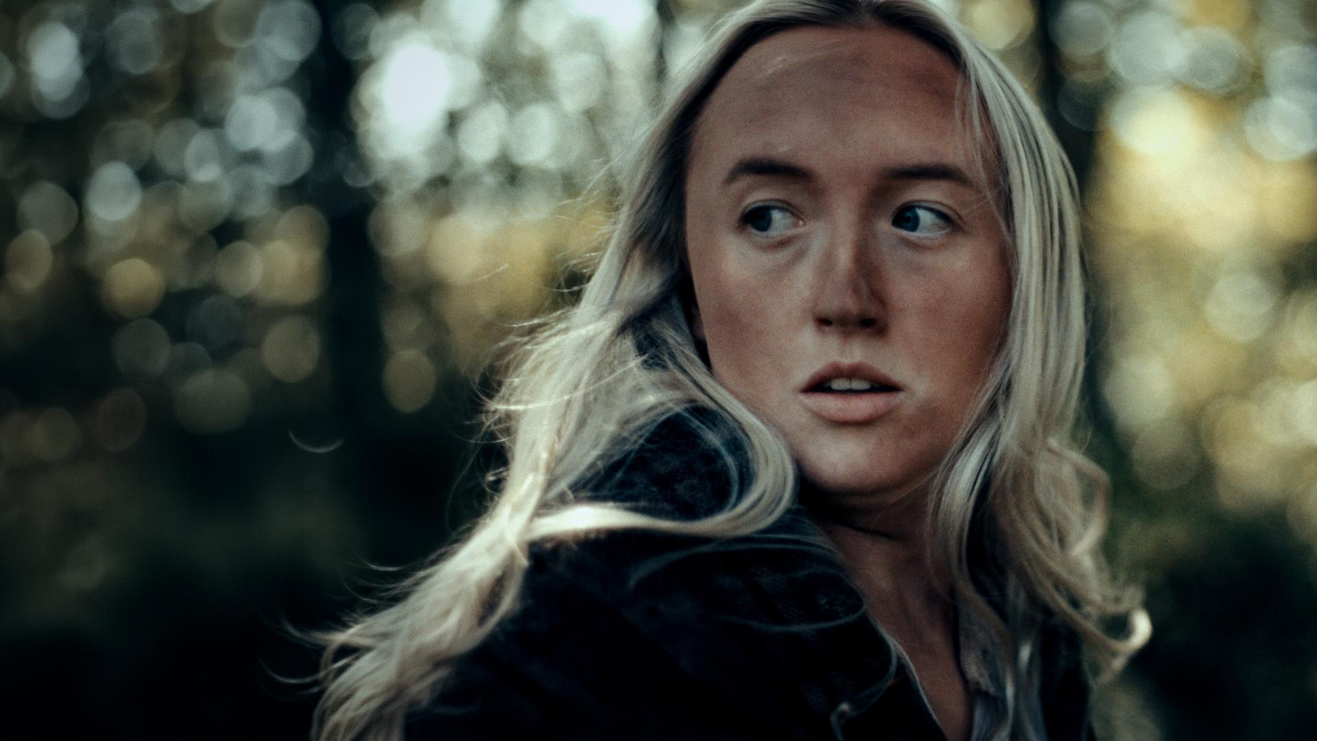 Portrait bis zur Brust, eine junge Frau mit langen blonden Haaren, dreckigem Gesicht, ihr Blick geht nach.