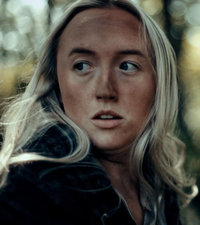 Portrait bis zur Brust, eine junge Frau mit langen blonden Haaren, dreckigem Gesicht, ihr Blick geht nach.
