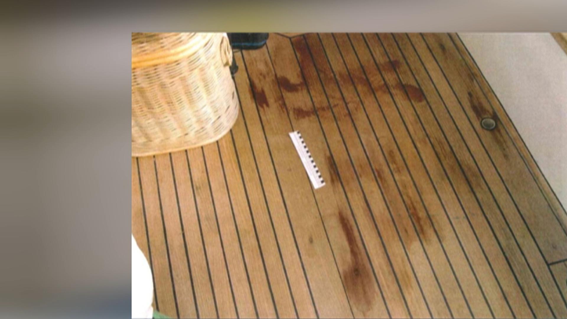 Auf einem braunen Holzboden sind rote Flecken sichtbar. Neben einem beigen Korb liegt ein weiß-schwarzes Lineal, das die Größe der Flecken misst.