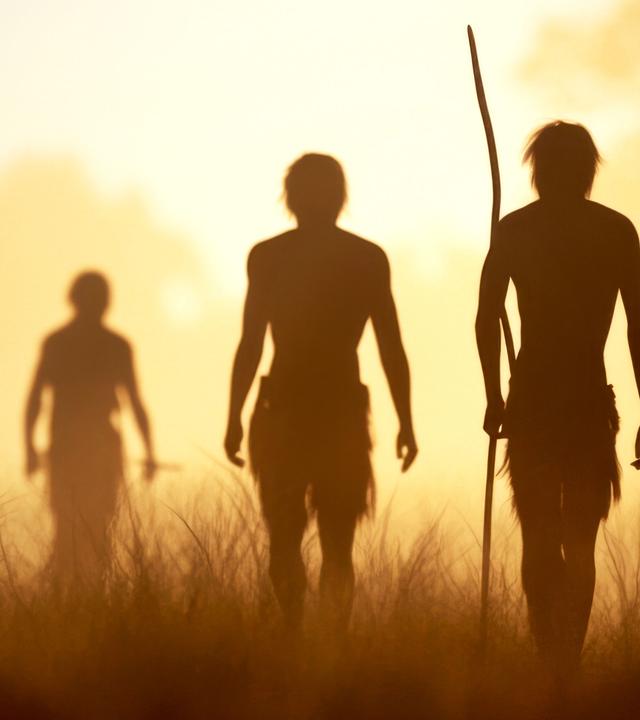 Eine Gruppe Urzeitmenschen in der Steppe, im Gegenlicht sind nur ihre Konturen zu erkennen