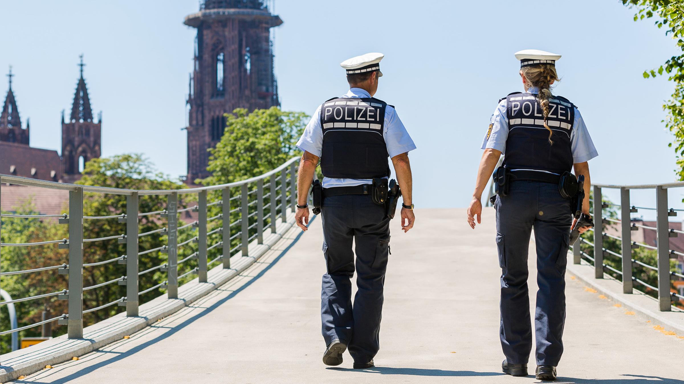 Zwei Polizisten, nur von hinten zu sehen, laufen nebeneinander über eine Brücke nahe des Freiburger Münsters