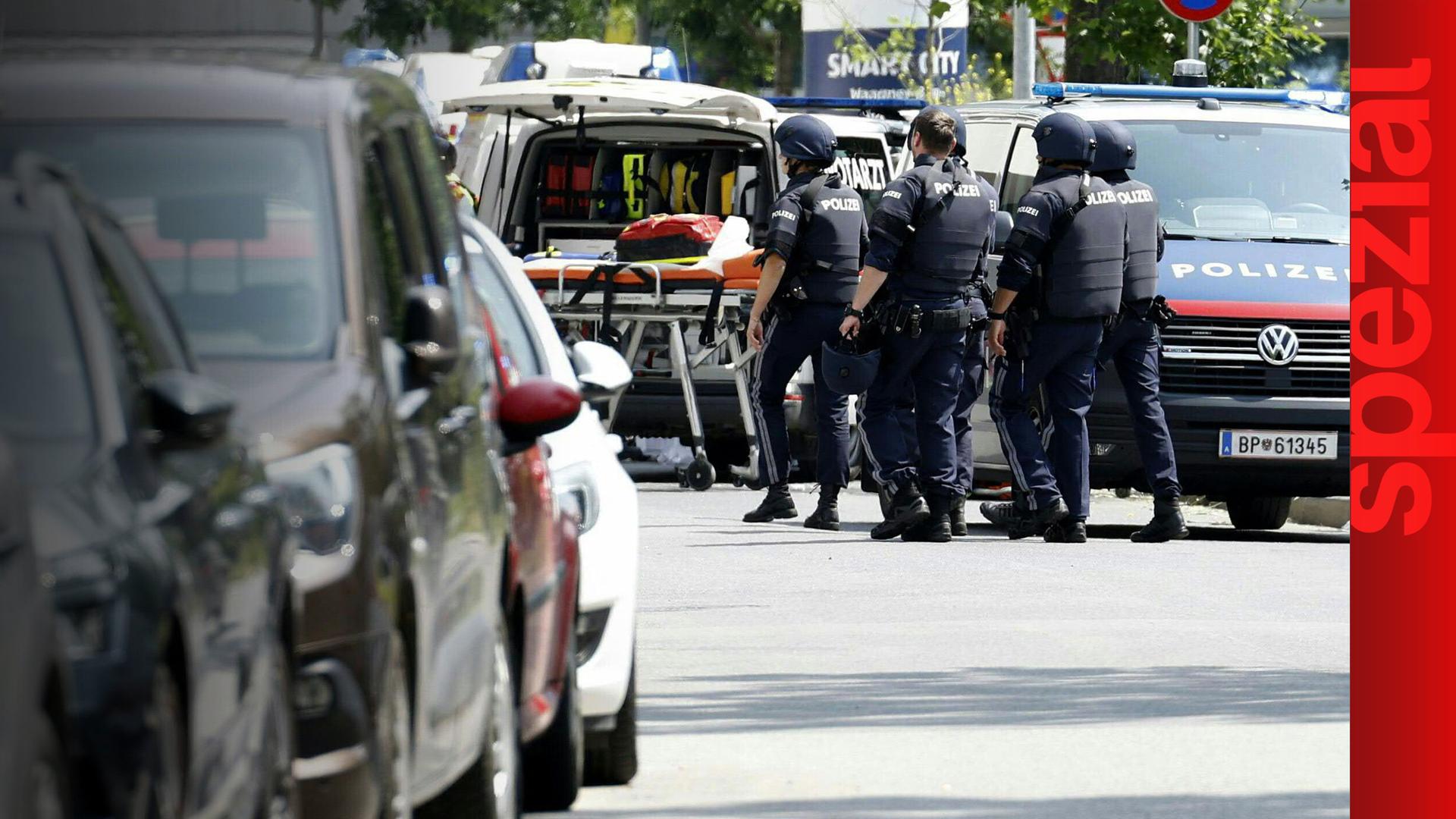 Polizisten am Tatort, zwischen einem Polizeiauto und einer Rettungsliege.