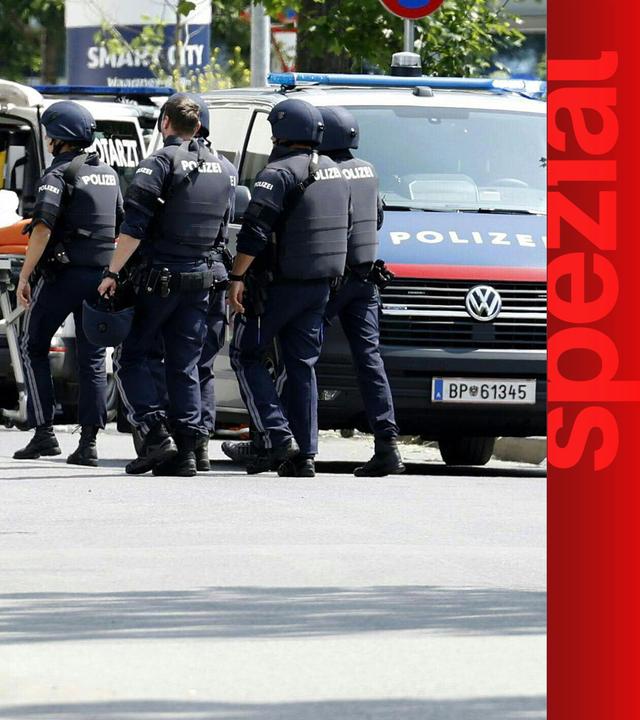 Polizisten am Tatort, zwischen einem Polizeiauto und einer Rettungsliege.