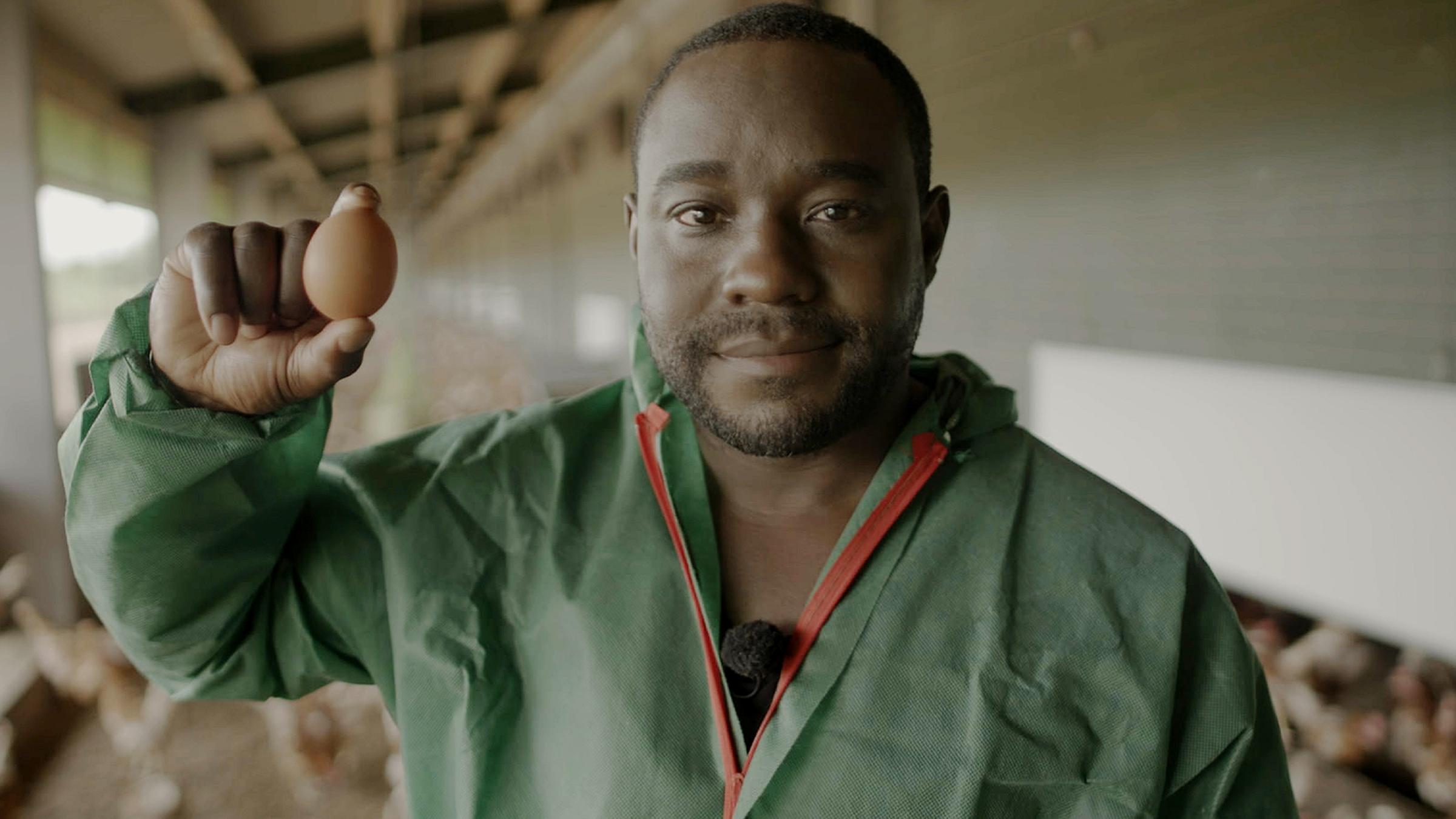 Nelson Müller steht in einem Stall und hält ein Ei in der Hand.