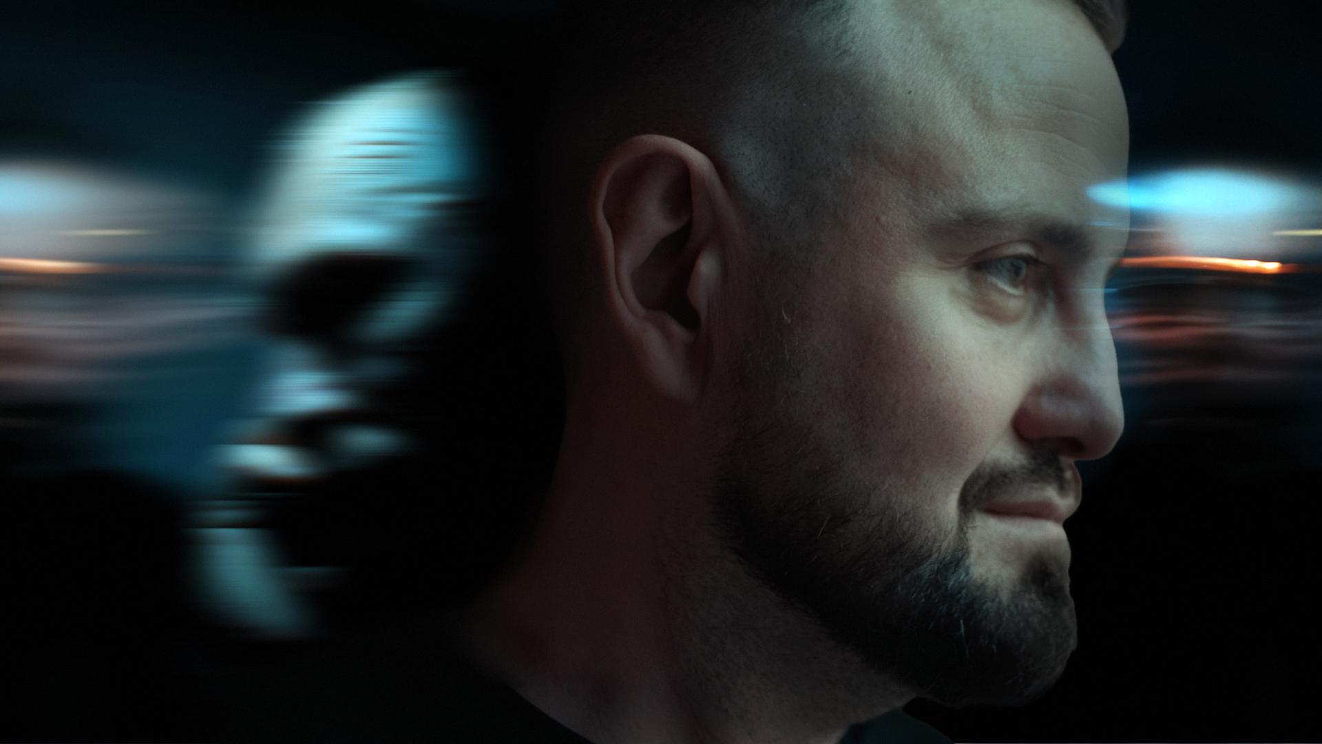 Collage mit zwei Gesichtern. Das eine ist im Profil nach rechts schauend - Hacker "BadB", ein Mann mit Glatze und Bart. Das andere Gesicht ist eher undeutlich als Profil nach links schauend im Hintergrund zu sehen.