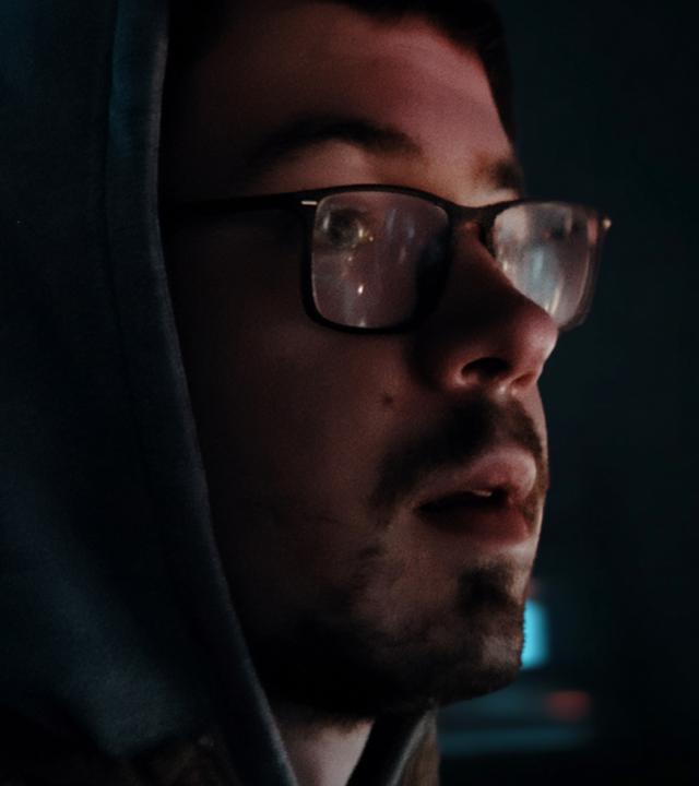 Eine Kollage mit zwei Gesichtern. Rechts im Vordergrund ein Mann mit Brille und Bart, der nach rechtshalboben schaut. Links und verschwommen Putins Gesicht.