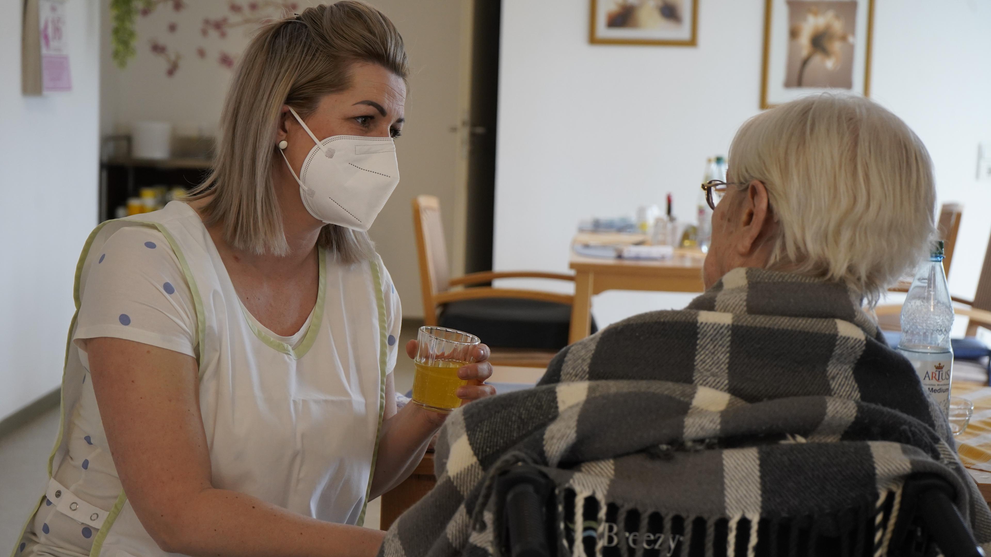 Eine Pflegerin reicht einer Seniorin ein Glas mit Saft