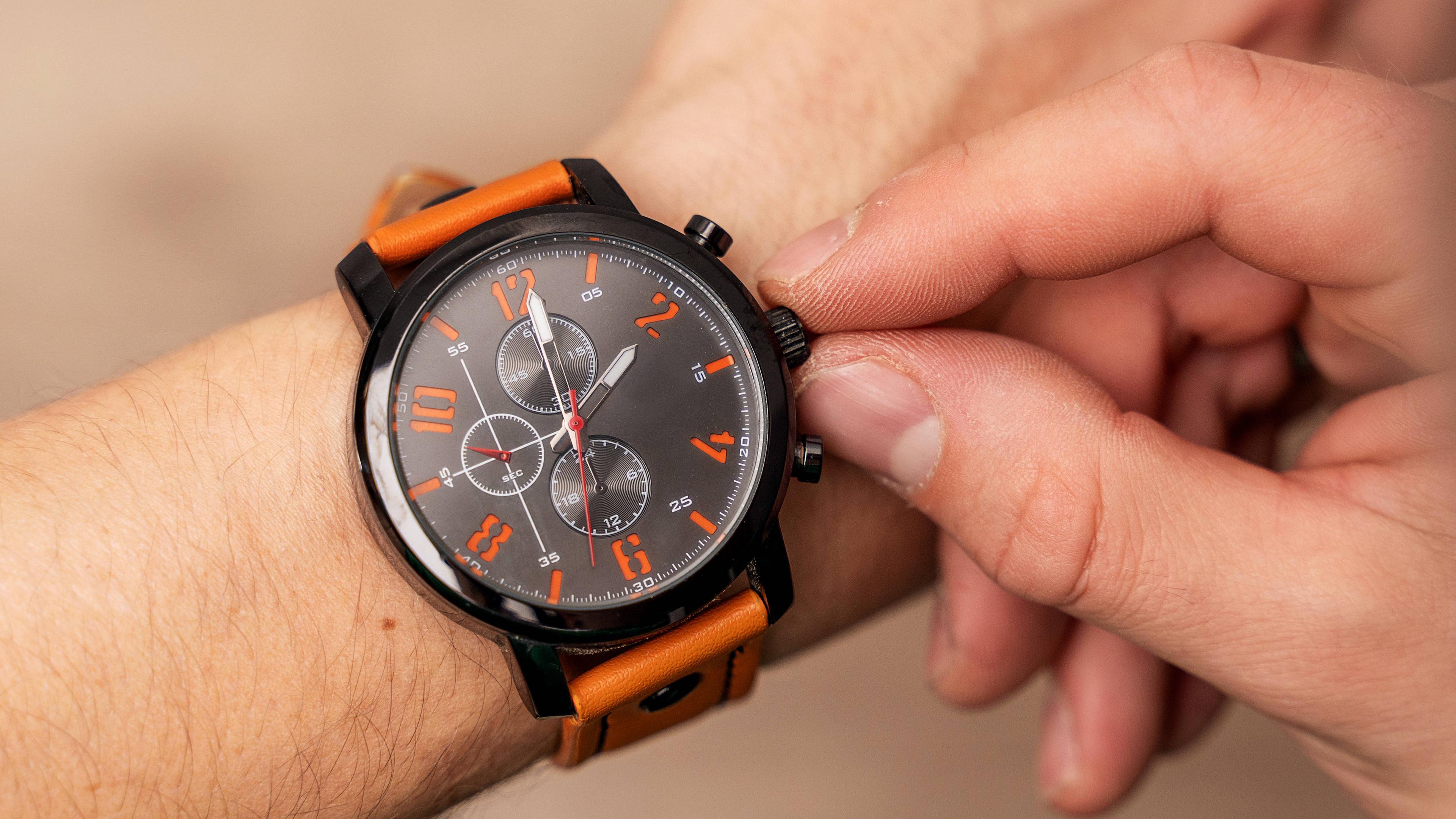 Ein Mann stellt auf seiner Armbanduhr die Zeit um. 