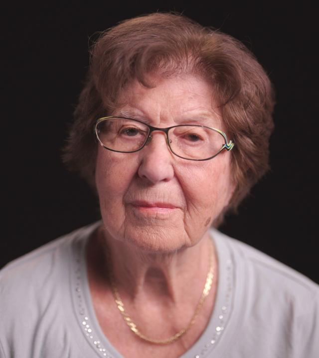 Holocaust Überlebende Ruth Pisarek frontal vor schwarzem Hintergrund.  