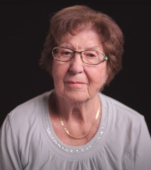 Holocaust Überlebende Ruth Pisarek frontal vor schwarzem Hintergrund.  