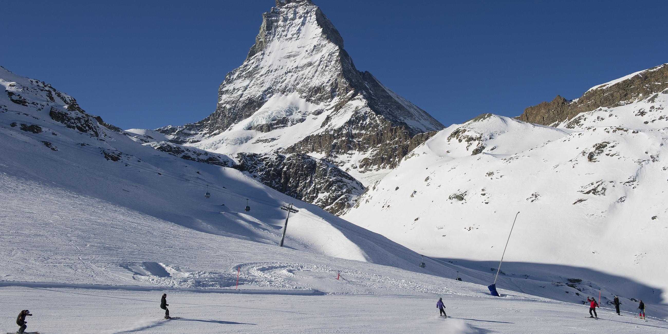 Skifahrer fahren die Pisten am Riffelberg mit dem Matterhorn im Hintergrund hinunter. 