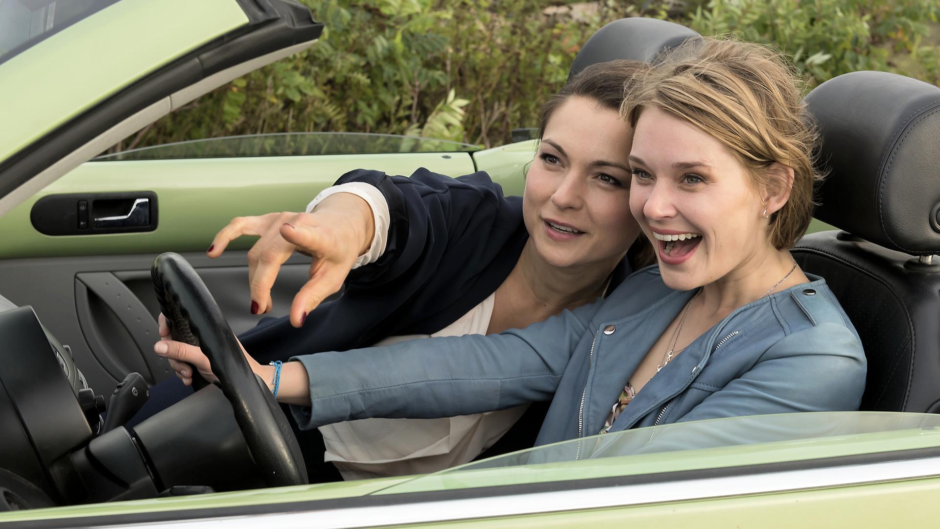 Paula (Henriette Richter-Röhl) und Emily (Nadja Bobyleva) fahren gut gelaunt in einem hellgrünen Cabrio auf einer Küstenstraße.