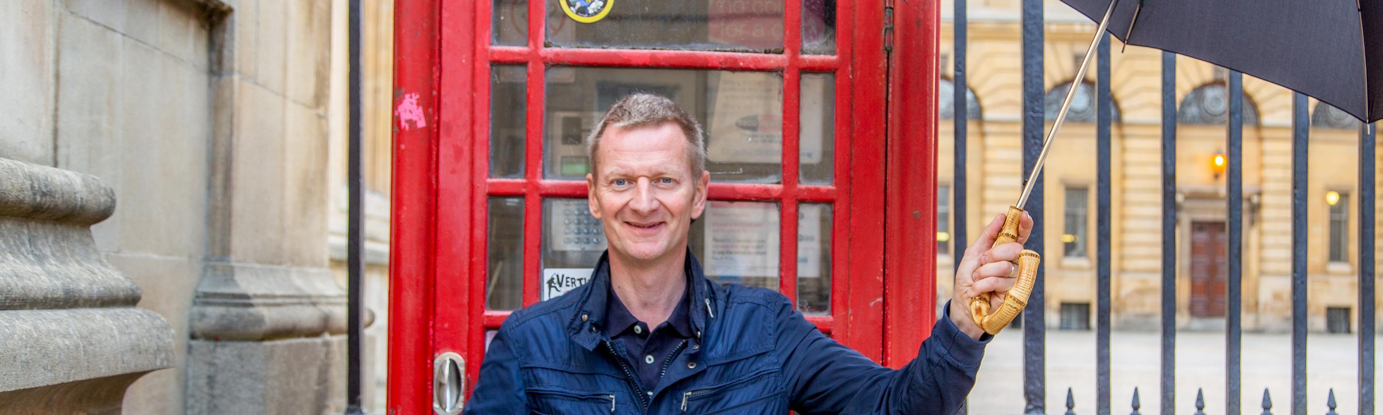 Michael Kessler mit Regenschirm vor einer englischen Telefonzelle