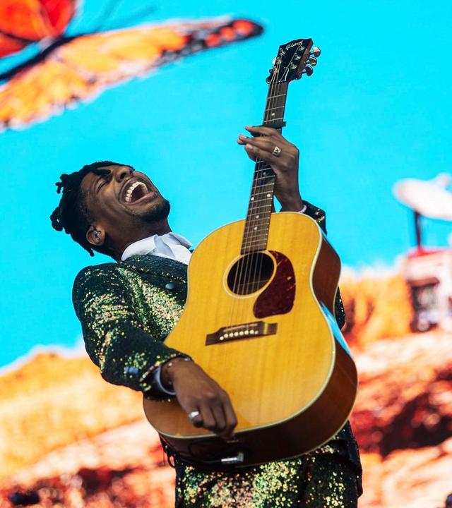 Ein Mann mit Gitarre in der Hand singt vor hellblauem Hintergrund. Links über ihm sieht man einen großen Schmetterling.
