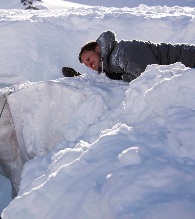 "Die Bergretter - Zu kurz gekommen (1)": Jan (Jan Hartmann) hängt in Skikleidung und mit Rucksack an einem Seil, über einem Abgrund im Schnee. Oberhalb liegt Niklas (Frederic Linkemann) und sieht ihn an.
