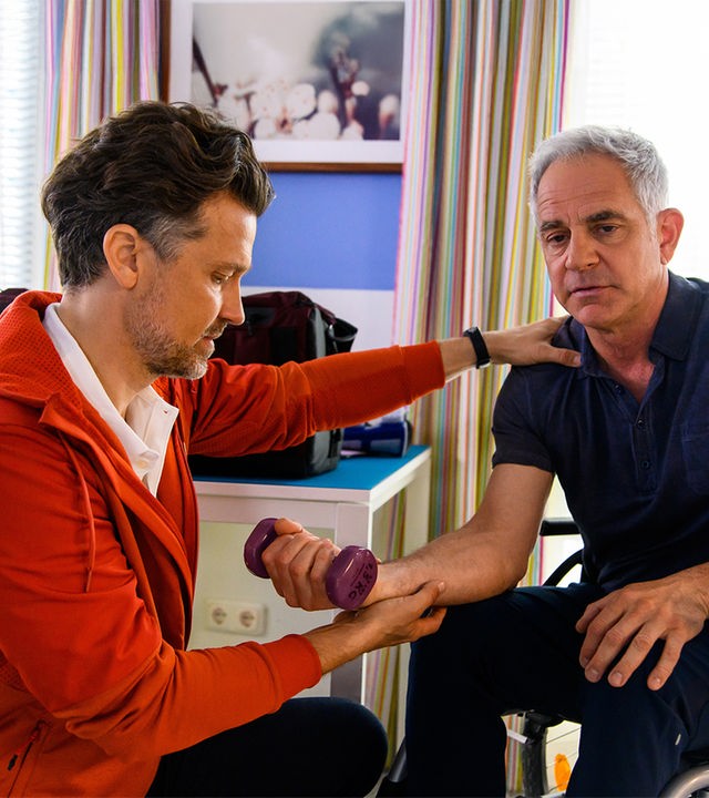 "Bettys Diagnose : Zu schnell zu viel": David Weber (Wayne Carpendale) macht mit Prof. Dr. Alexander von Arnstett (Florian Fitz), der im Rollstuhl sitzt, Hanteltraining.
