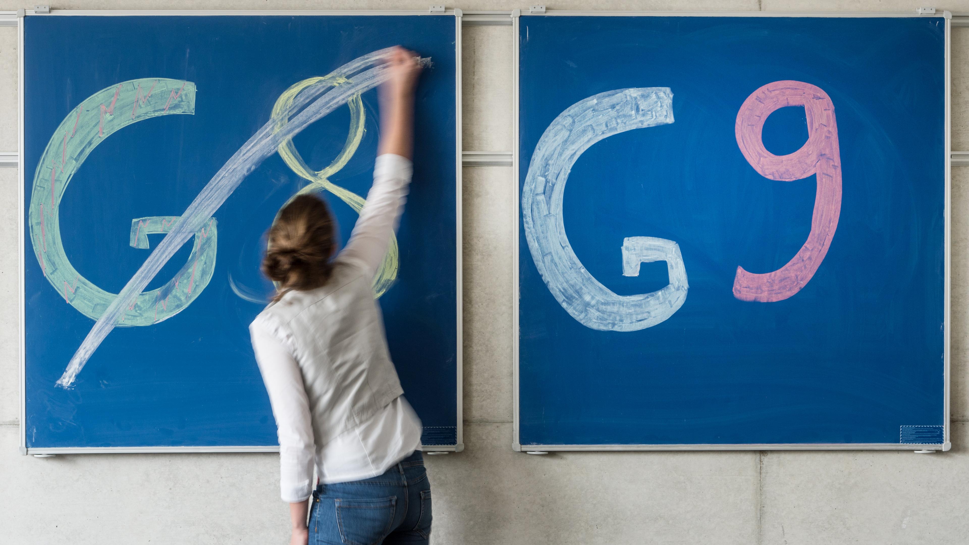 Eine Schülern der Oberstufe streicht an einem Gymnasium den Schriftzug "G8" an einer Tafel durch, daneben lässt sie "G9" unberührt.