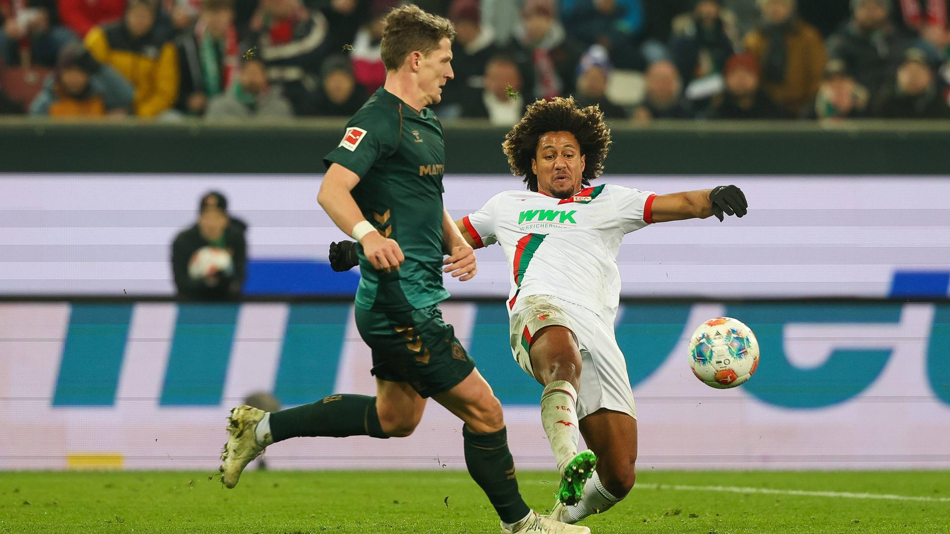 Augsburgs Han-Noah Massengo grätscht im Zweikampf mit Bremens Jens Stage in Richtung Ball um seinen Gegenspieler zu stoppen