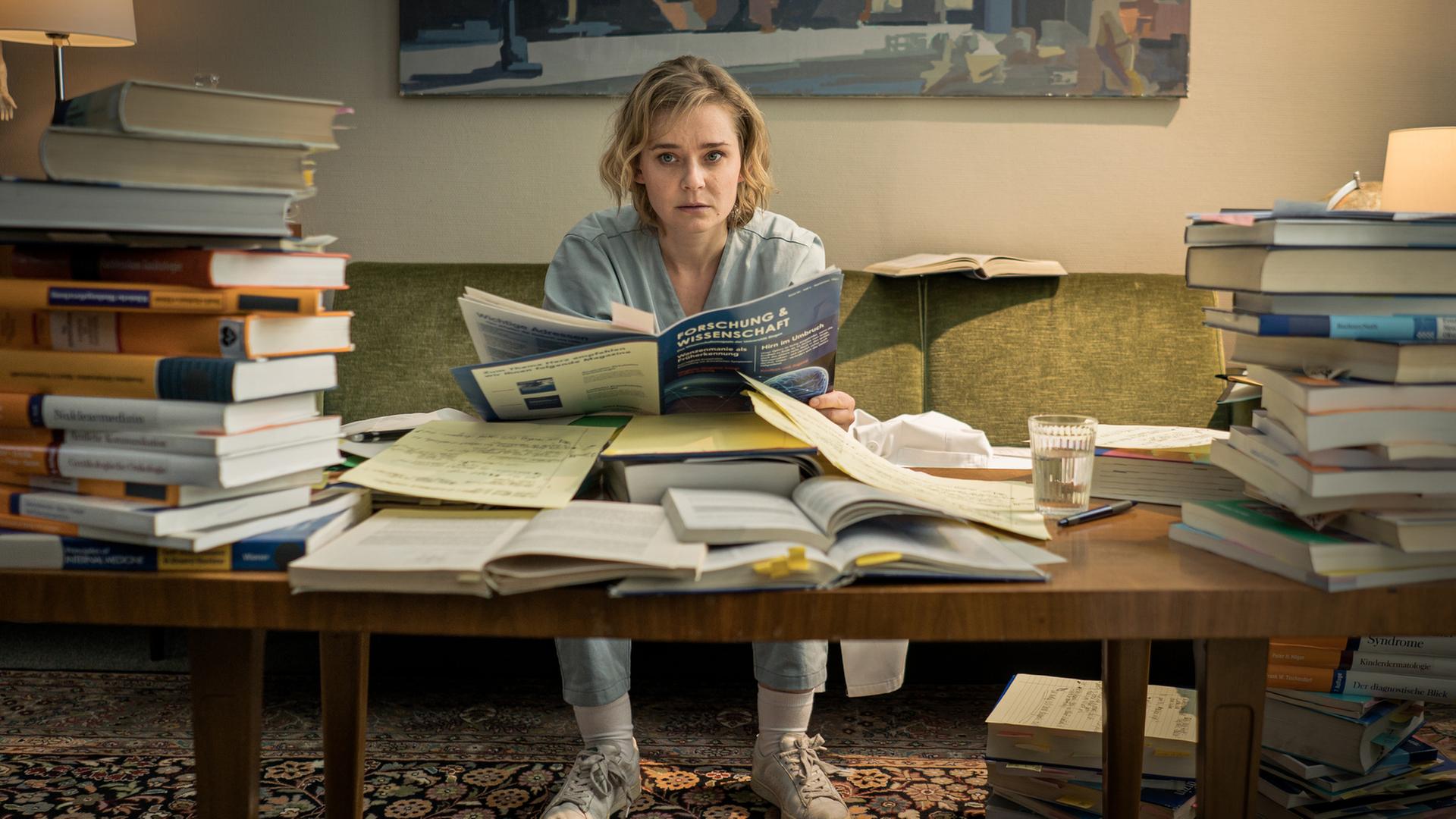 "Doktor Ballouz - Zweite Chance": Dr. Michelle Schwan (Nadja Bobyleva) sitzt vor Unmengen an gestapelten medizinischen Büchern an einem Tisch auf dem Sofa.
