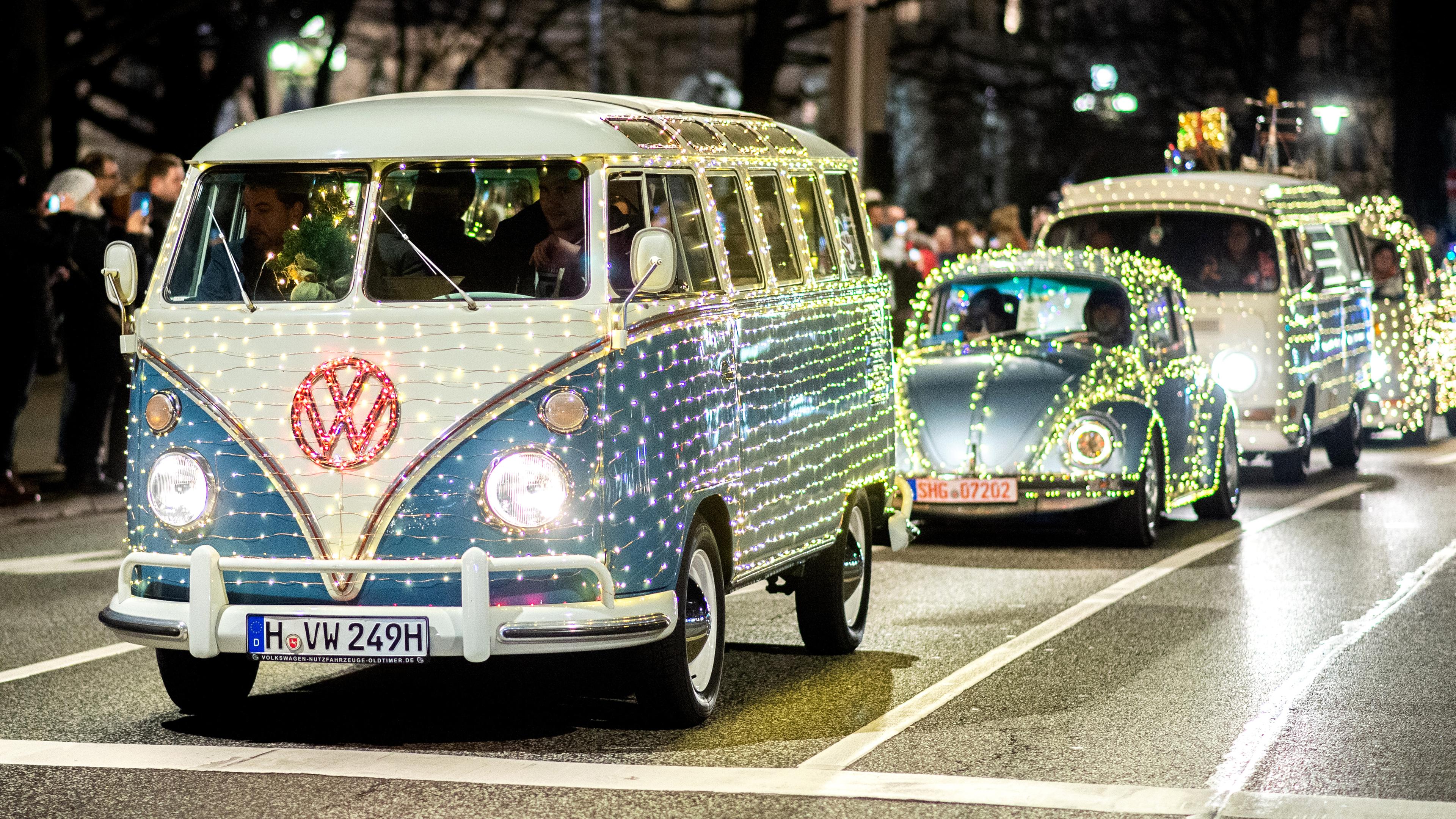Mehrere mit Lichterketten geschmückte Volkswagen vom Typ Bulli und Käfer fahren durch die Innenstadt von Hannover.