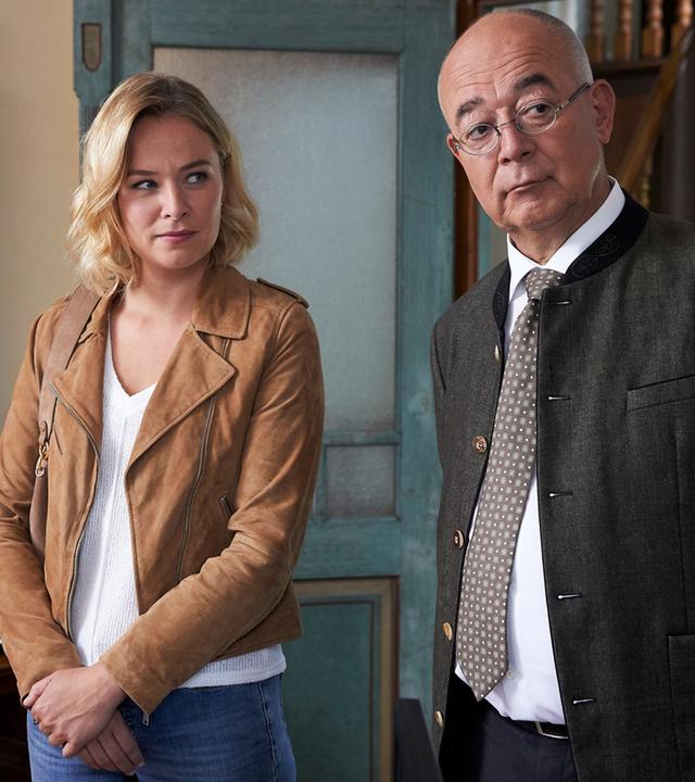 "Die Rosenheim-Cops - Ein Zwilling kommt selten allein": Kommissarin Winter (Vanessa Eckart) und Polizeidirektor Achtziger (Alexander Duda) stehen nebeneinander in einem Wohnraum. Achtziger schaut zur Seite, während Kommissarin Winter ihn ansieht.