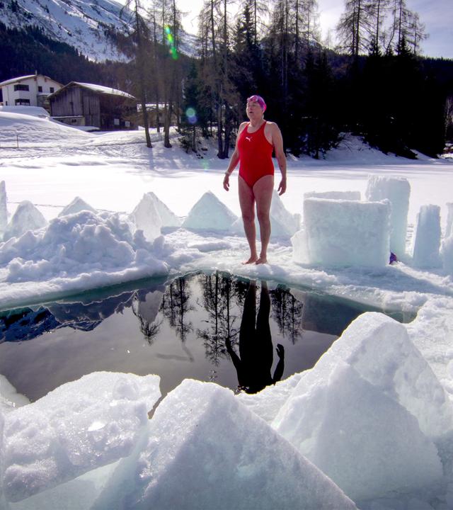 Eine Frau steht vor einem Loch in einem eingefrorenen See im Badeanzug.