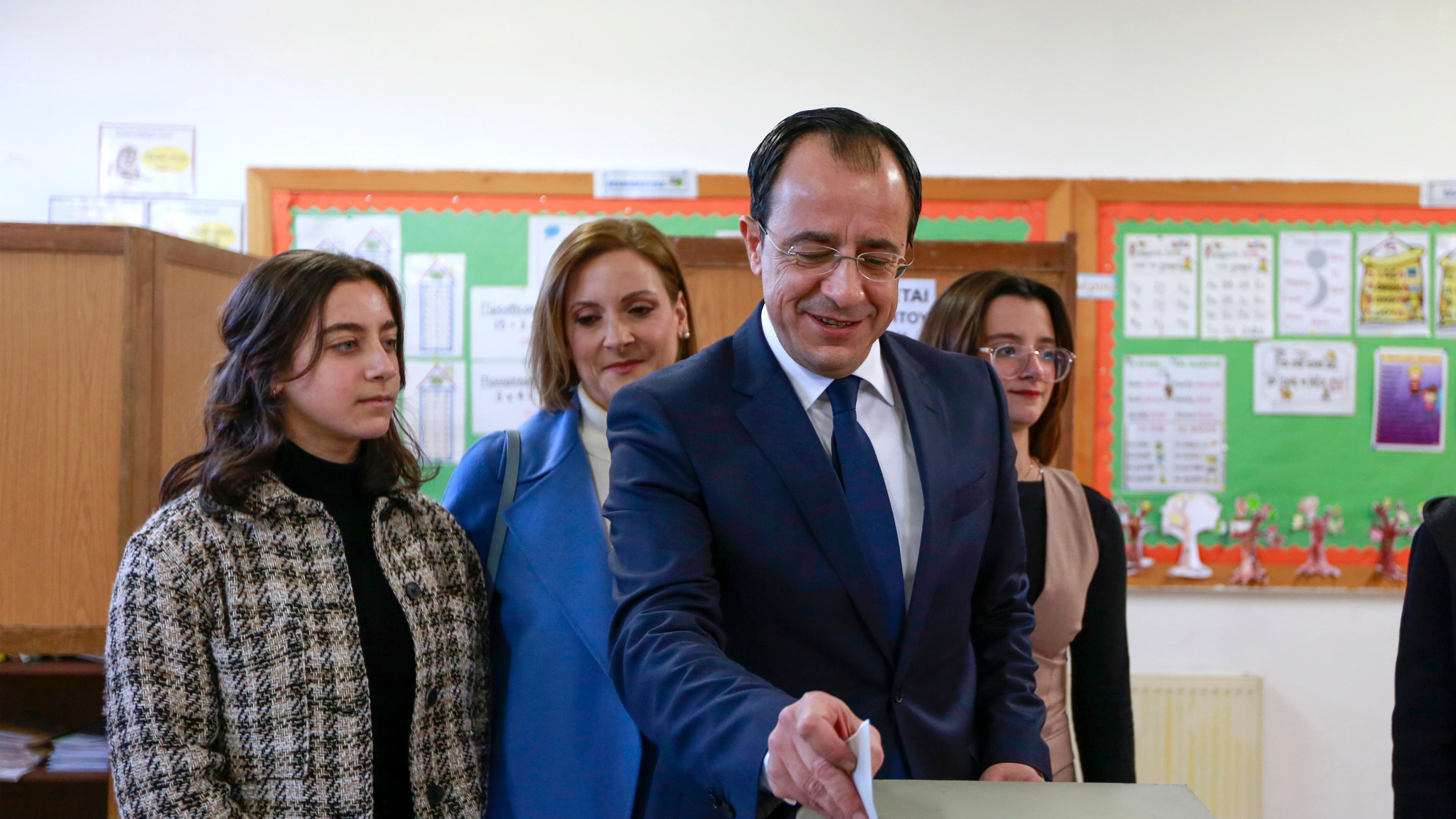 Nikos Christodoulides schiebt seinen Wahlzettel in eine Wahlurne. Um ihn herum stehen Mädchen aus seiner Familie und eine Frau.